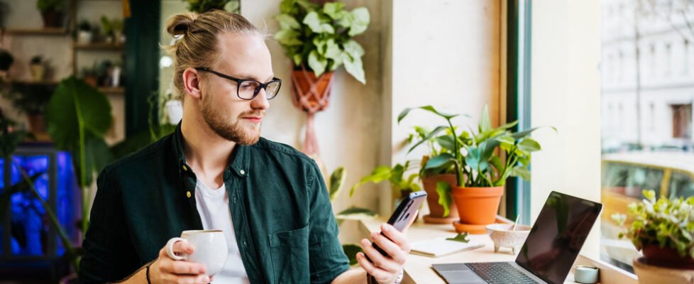 A student using his smartphone while taking a break from work with a coffee in a local café.